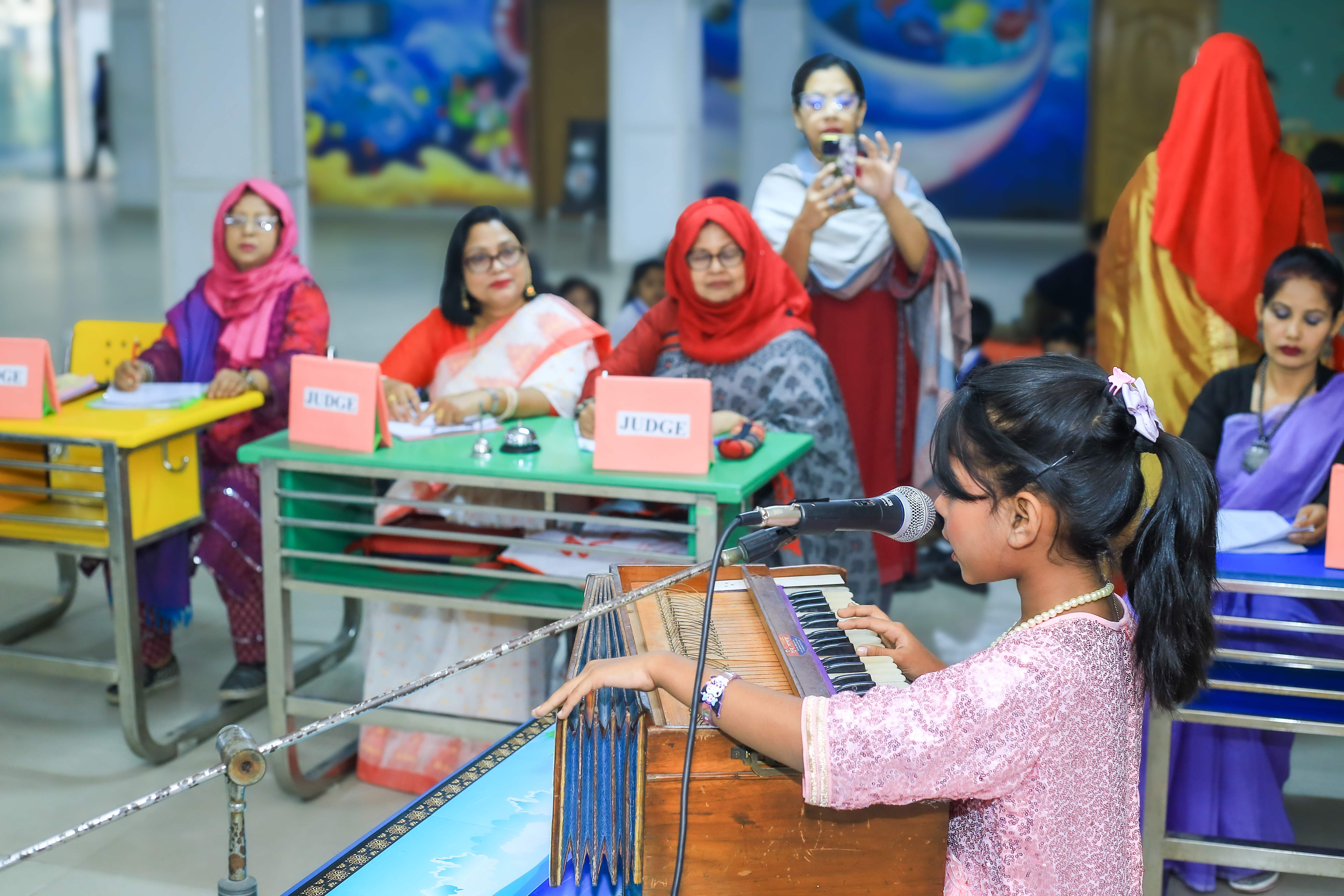 A student performer in the foreground with judges seated behind her during the event